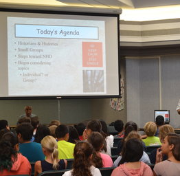 teacher presenting to students next to a screen
